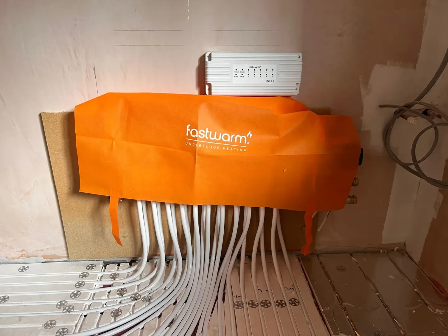 Underfloor heating manifold with protective cover and pipe loops feeding into the floor