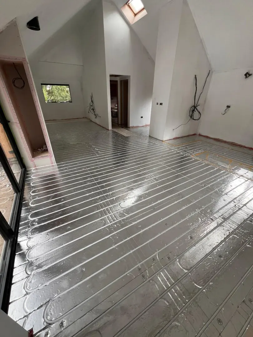 Underfloor heating pipe loops laid in aluminium spreader plates across an open-plan room