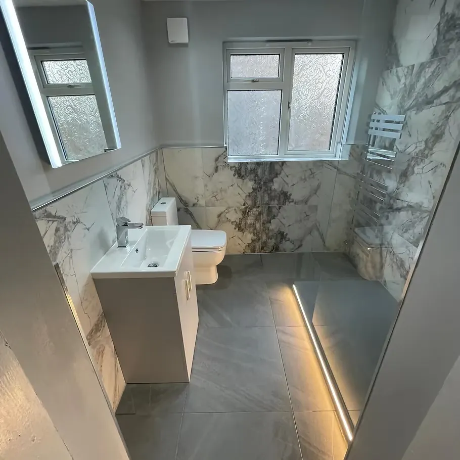 Marble-panelled bathroom with LED-lit bath plinth, white toilet and basin